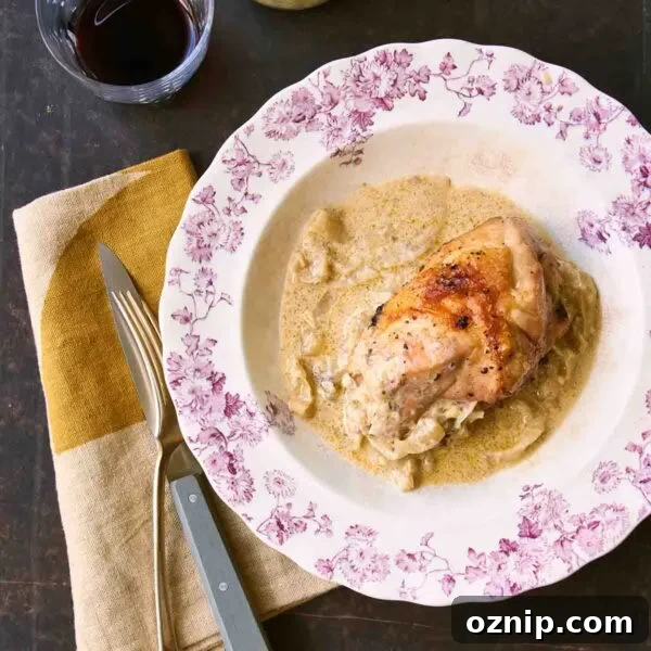A floral-patterned plate topped with a piece of roast chicken with onion gravy around it and a fork, knife, and napkin on the side.