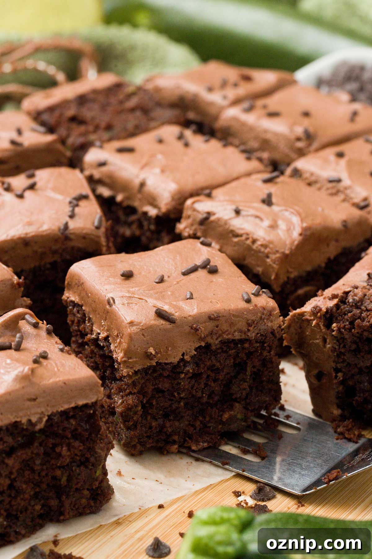 A close up of gluten-free chocolate zucchini cake with chocolate cream cheese frosting and sprinkles on top.