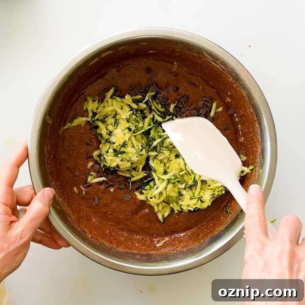 Folding in the shredded zucchini and mini chocolate chips to the cake batter.