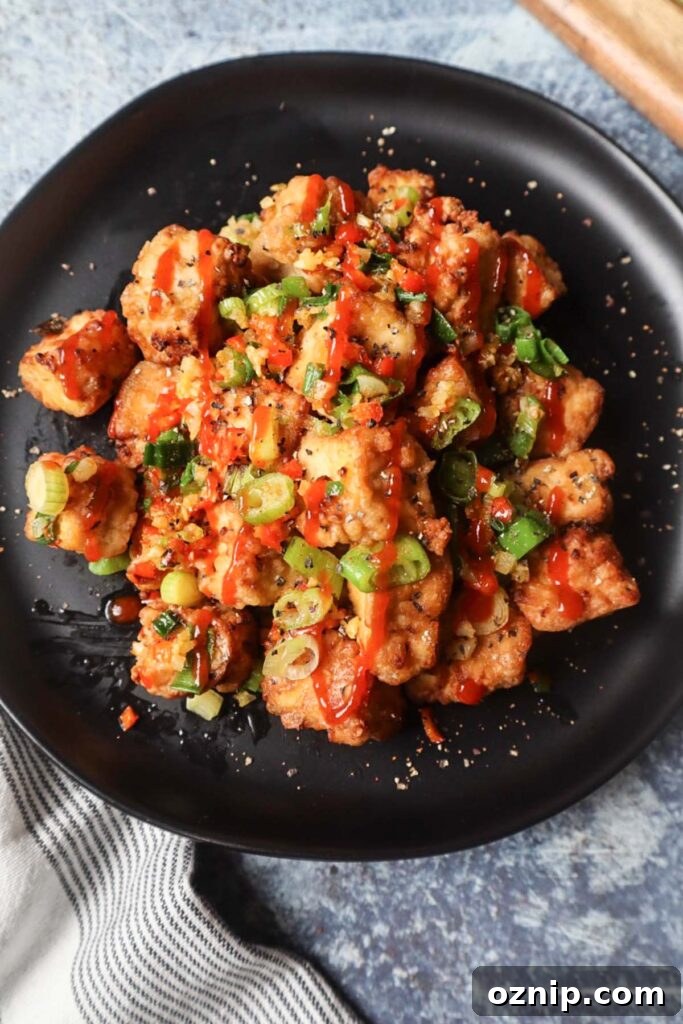 Crispy Salt and Pepper Tofu in the Air Fryer 2 black plate with salt and pepper tofu topped with green onion, red chili pepper, and garlic