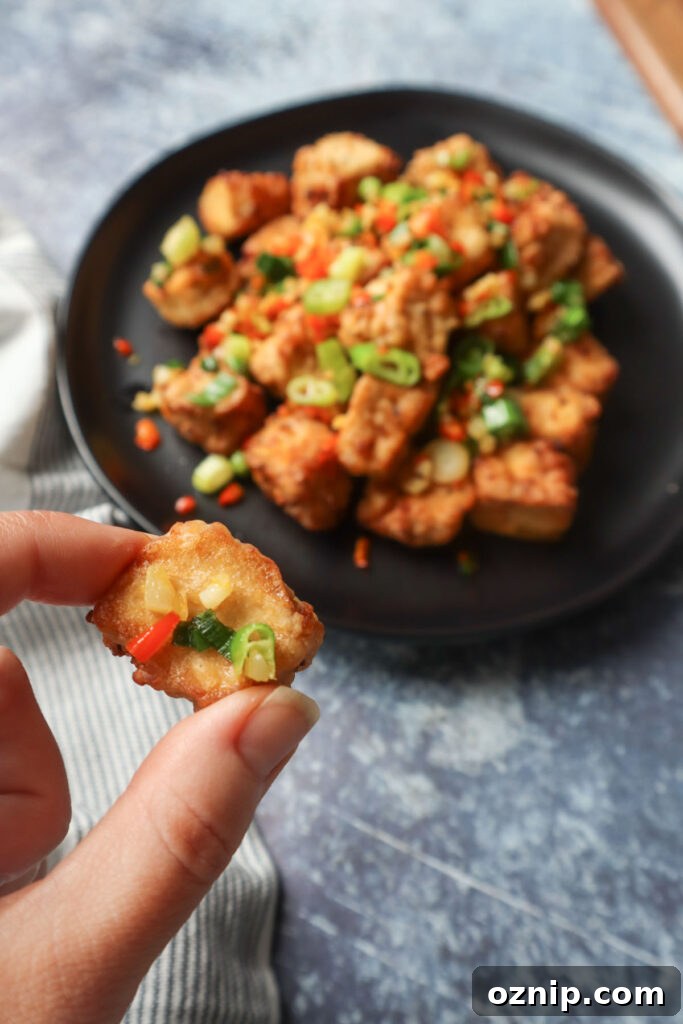 Crispy Salt and Pepper Tofu in the Air Fryer 5 hand holding air fryer salt and pepper tofu topepd with green onion, thai chili, and garlic