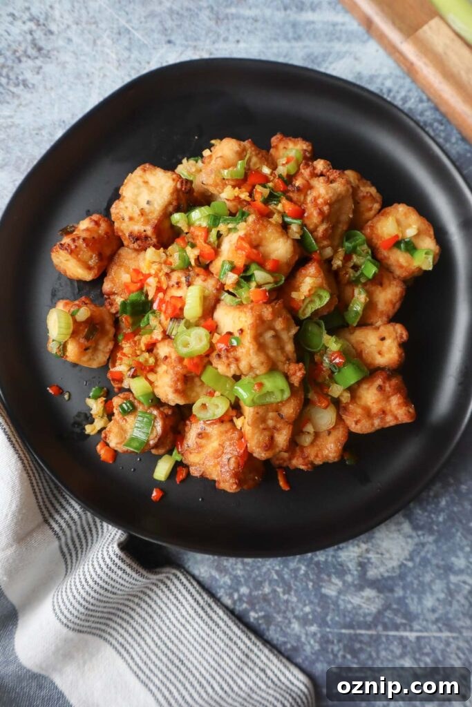 Crispy Salt and Pepper Tofu in the Air Fryer 6 black plate with salt and pepper tofu topped with green onion, red chili pepper, and garlic
