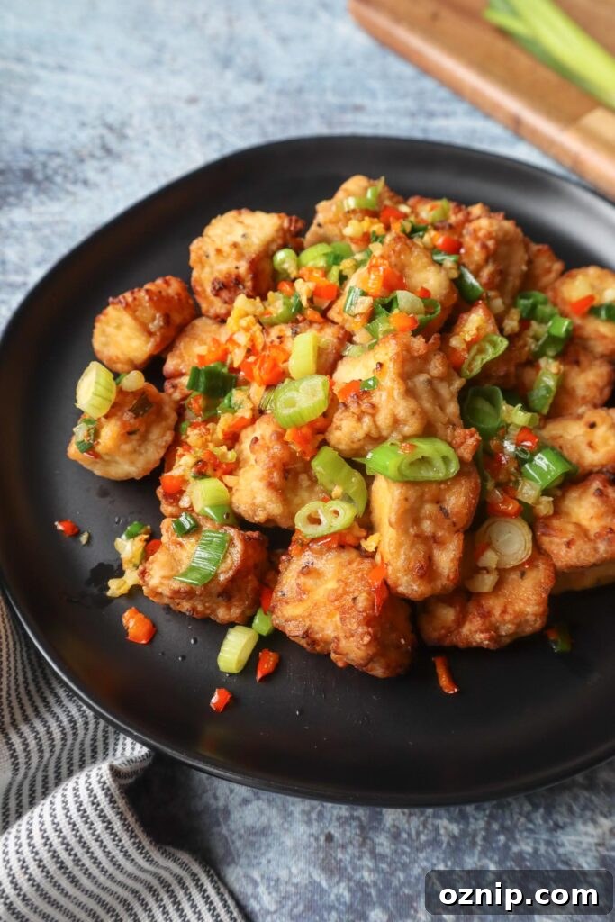 Crispy Salt and Pepper Tofu in the Air Fryer 7 black plate with salt and pepper tofu topped with green onion, red chili pepper, and garlic