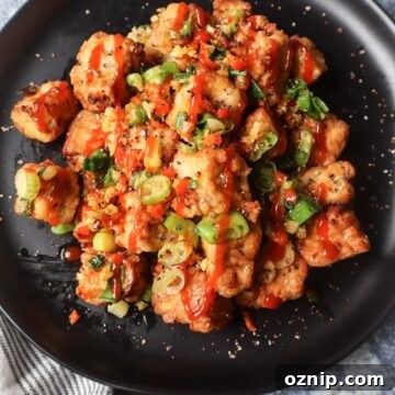 Crispy Salt and Pepper Tofu in the Air Fryer 8 black plate with salt and pepper tofu topped with green onion, red chili pepper, and garlic