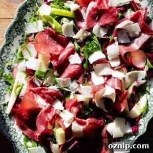 A close up of a bresaola salad topped with shavings of Parmigiano Reggiano on a servings plate.