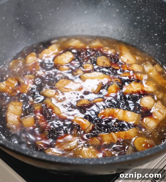 Chinese Red Braised Pork Belly Recipe 8 Braised pork belly simmering uncovered as the sauce reduces and thickens, turning glossy and coating each piece with a sticky soy glaze.