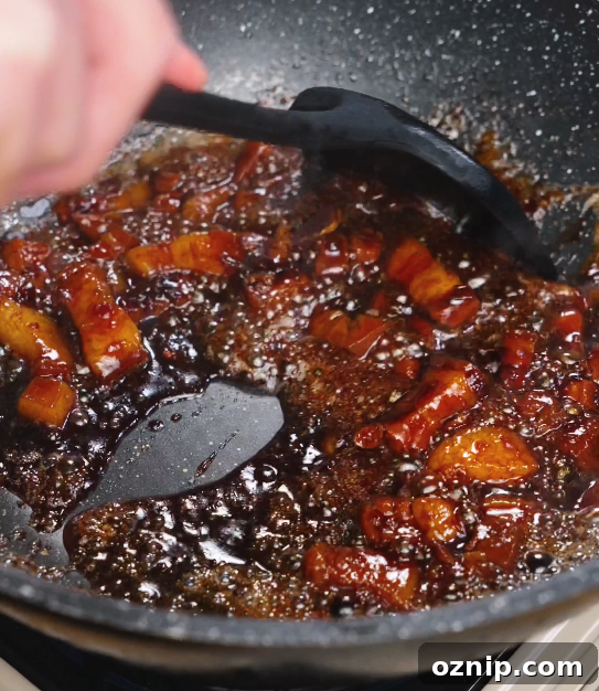 Chinese Red Braised Pork Belly Recipe 9 Pork belly being stirred through a thickened, bubbling sauce as the glaze clings to the meat, creating a rich, lacquered finish.