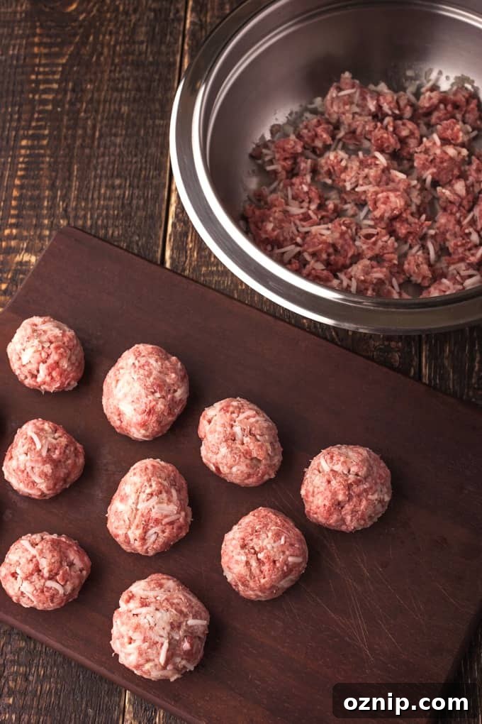 Meatballs on a dark brown wood board with meatball mixture in a pan on the side