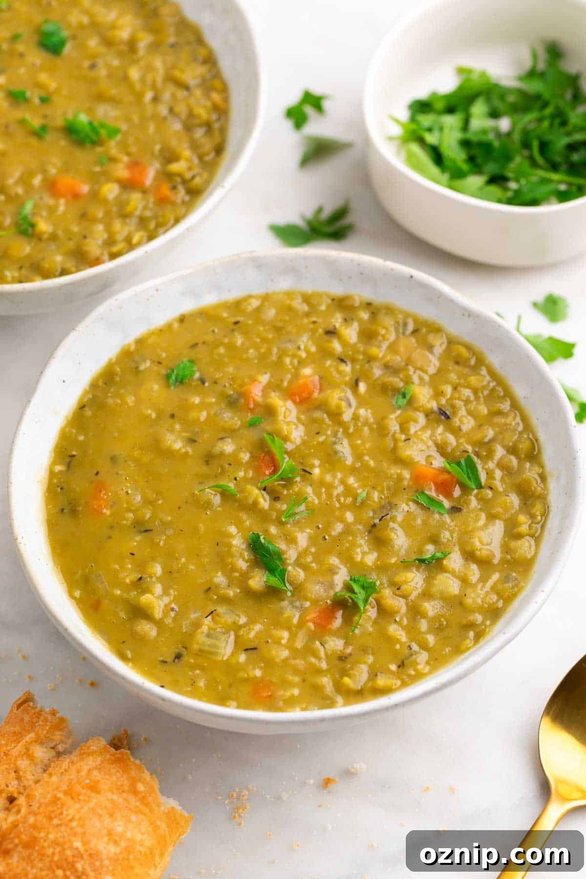 Hearty Vegan Split Pea Soup Recipe 2 Two bowls of split pea soup with a spoon, bread, and parsley.