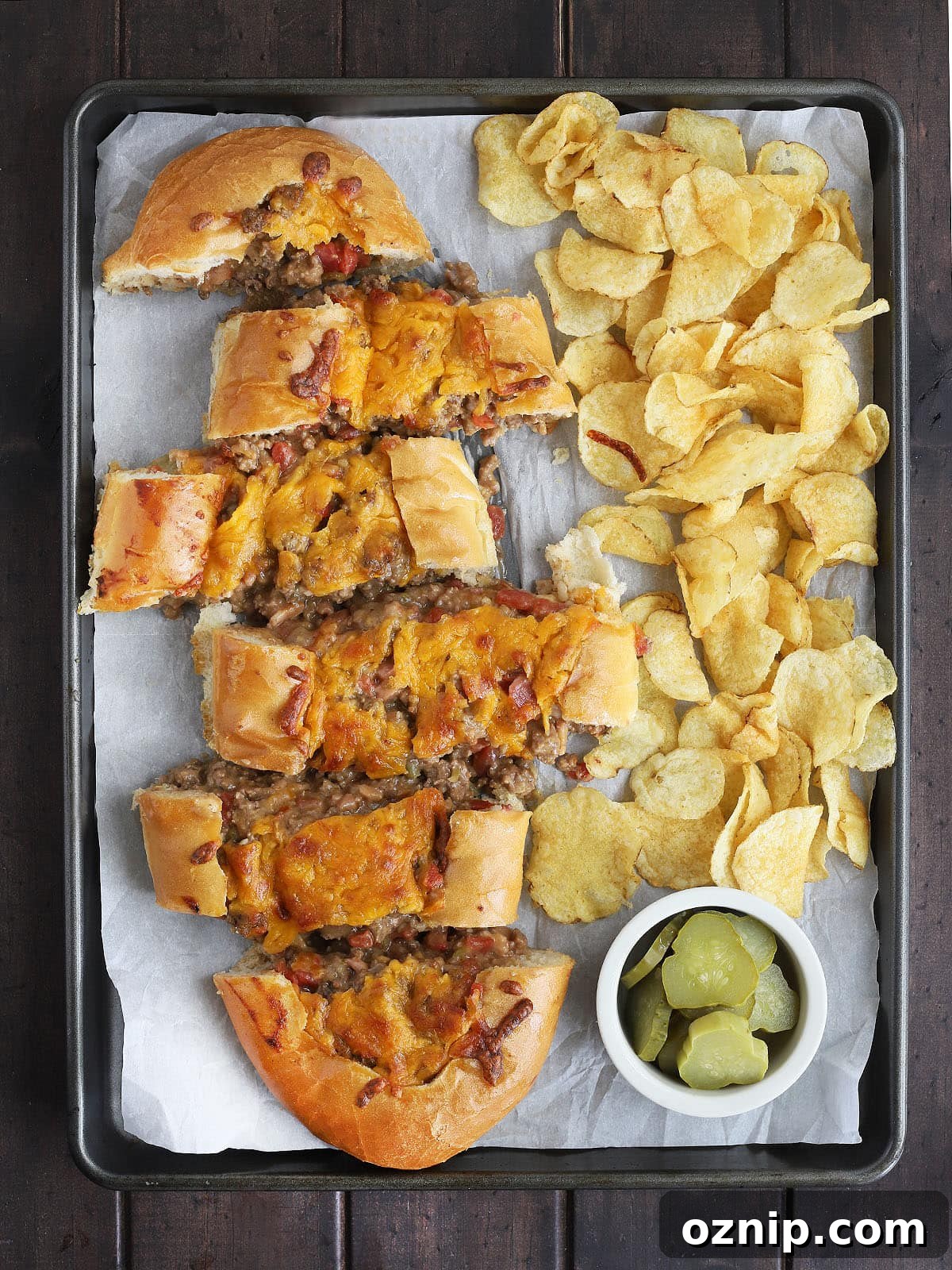 Bacon Cheeseburger Stuffed French Bread Recipe 2 sliced bacon cheeseburger stuffed French bread on a parchment paper lined baking sheet