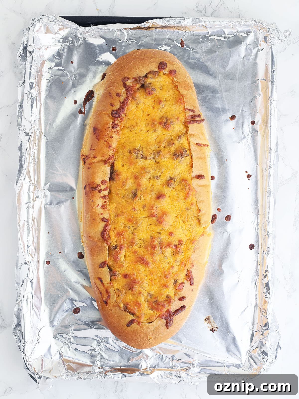 Bacon Cheeseburger Stuffed French Bread Recipe 13 baked bacon cheeseburger stuffed French bread on a foil lined baking sheet