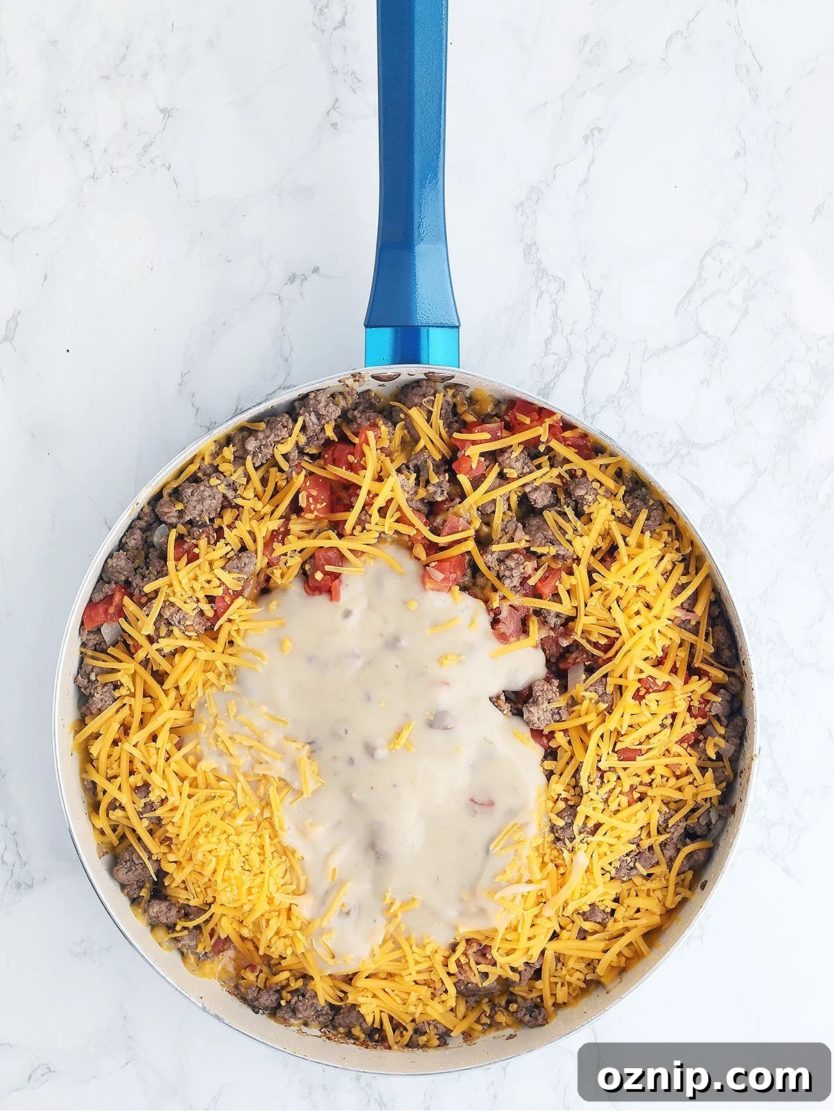 Bacon Cheeseburger Stuffed French Bread Recipe 8 browned burger, tomatoes, soup mixture and shredded cheese in a blue skillet