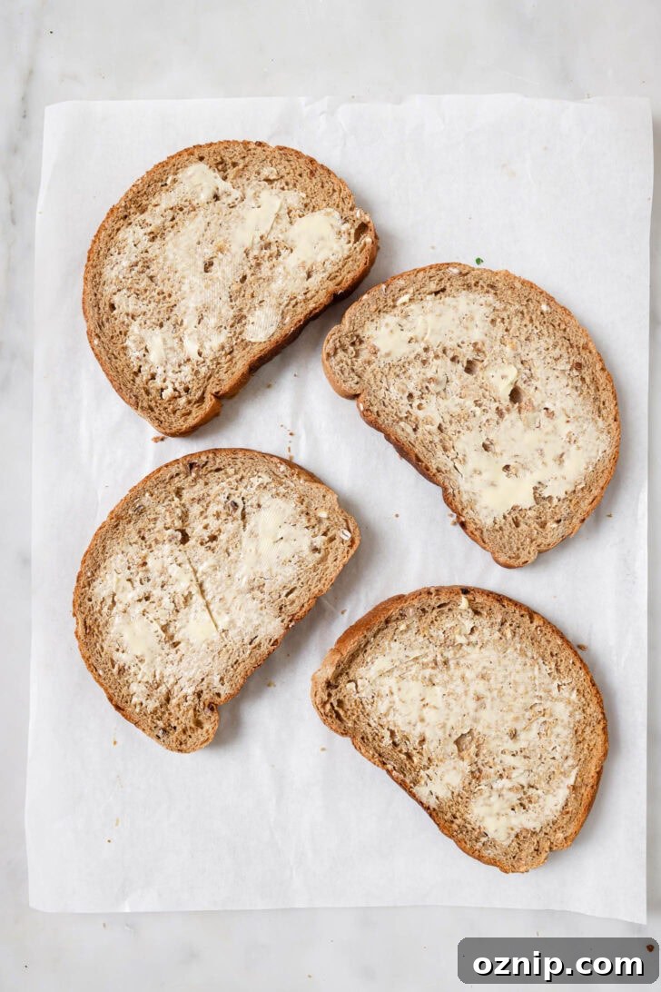 Slices of buttered multigrain bread on a piece of parchment paper ready for making Chicken Sandwiches.