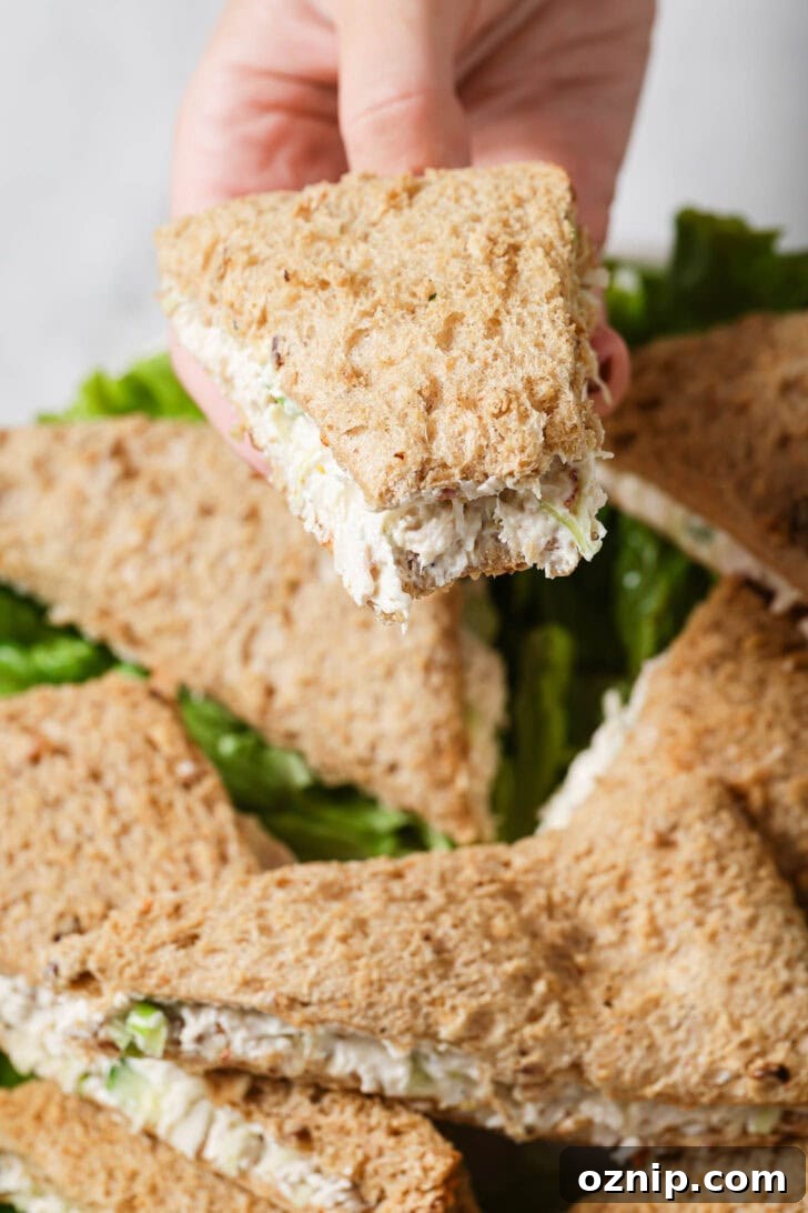 Holding a partially eaten Chicken Sandwich over a platter of sandwiches.
