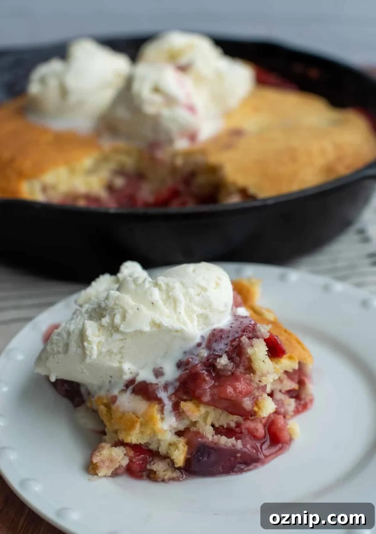 A slice of strawberry cobbler on a plate is topped with ice cream.