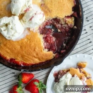 Strawberry sourdough cobbler in a skillet on a table with some on a plate and ice cream on top.