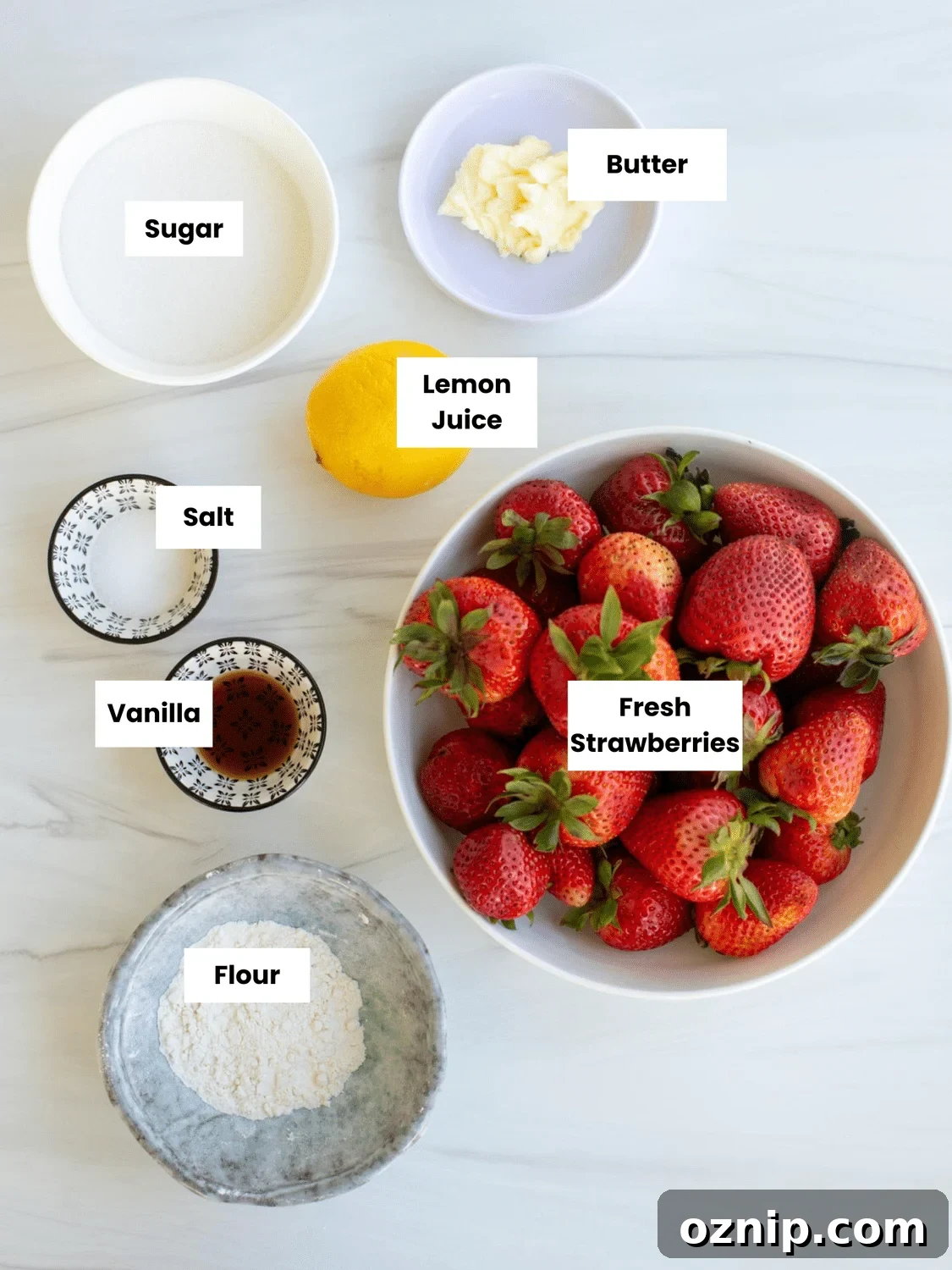 Cobbler filling ingredients on a countertop include sugar, butter, lemon juice, salt, vanilla, fresh strawberries, and flour.