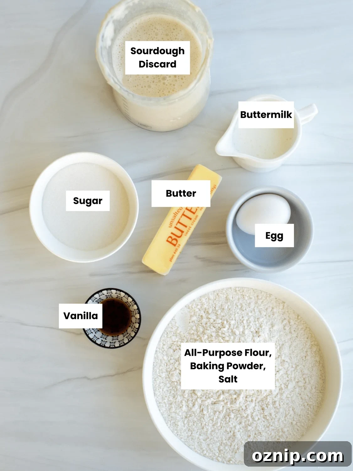 Cobbler topping ingredients on a counter include sourdough discard, buttermilk, sugar, butter, an egg, vanilla, flour, baking powder, and salt.