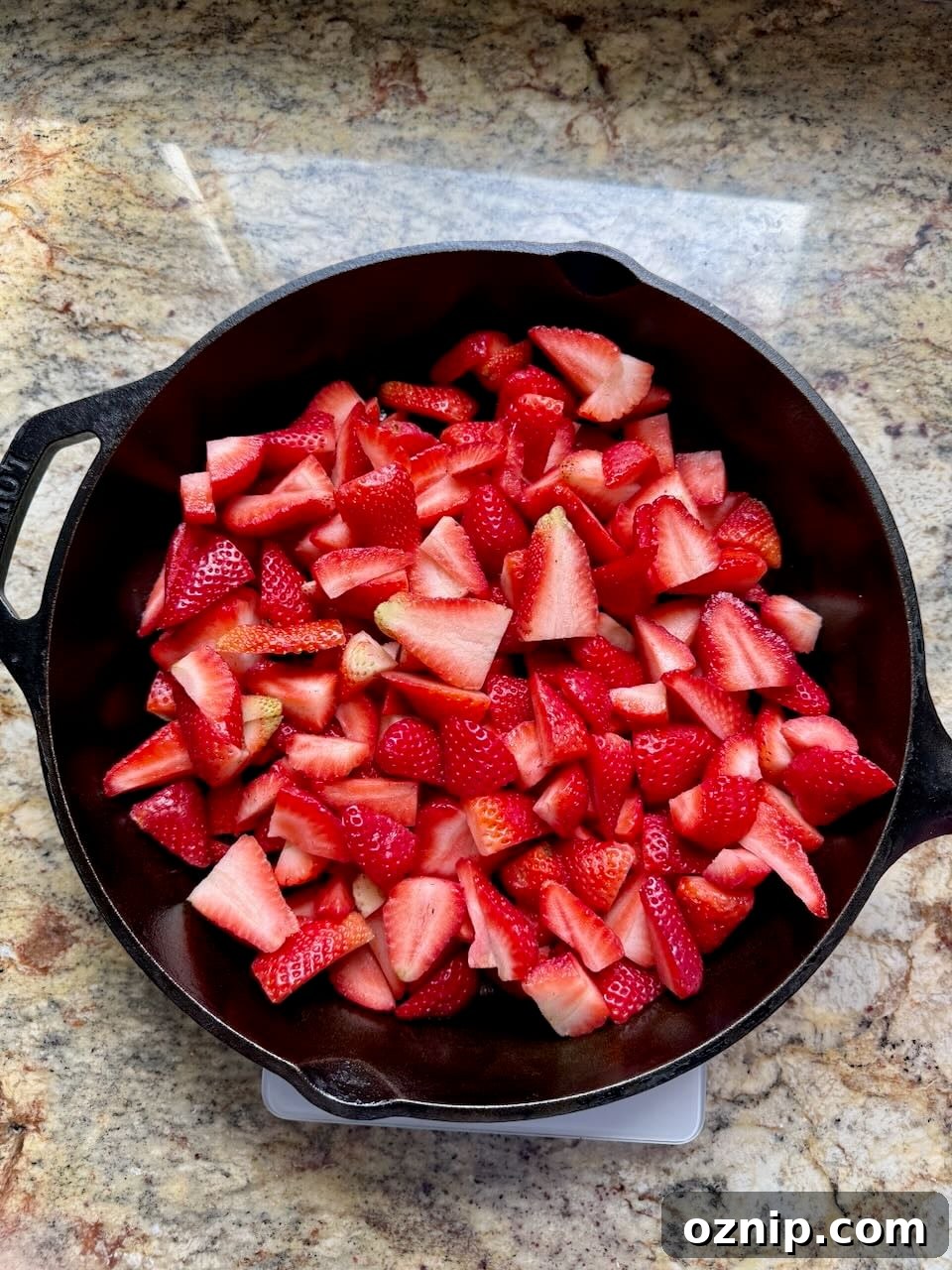 Freshly sliced strawberries are sitting in a cast iron skillet.