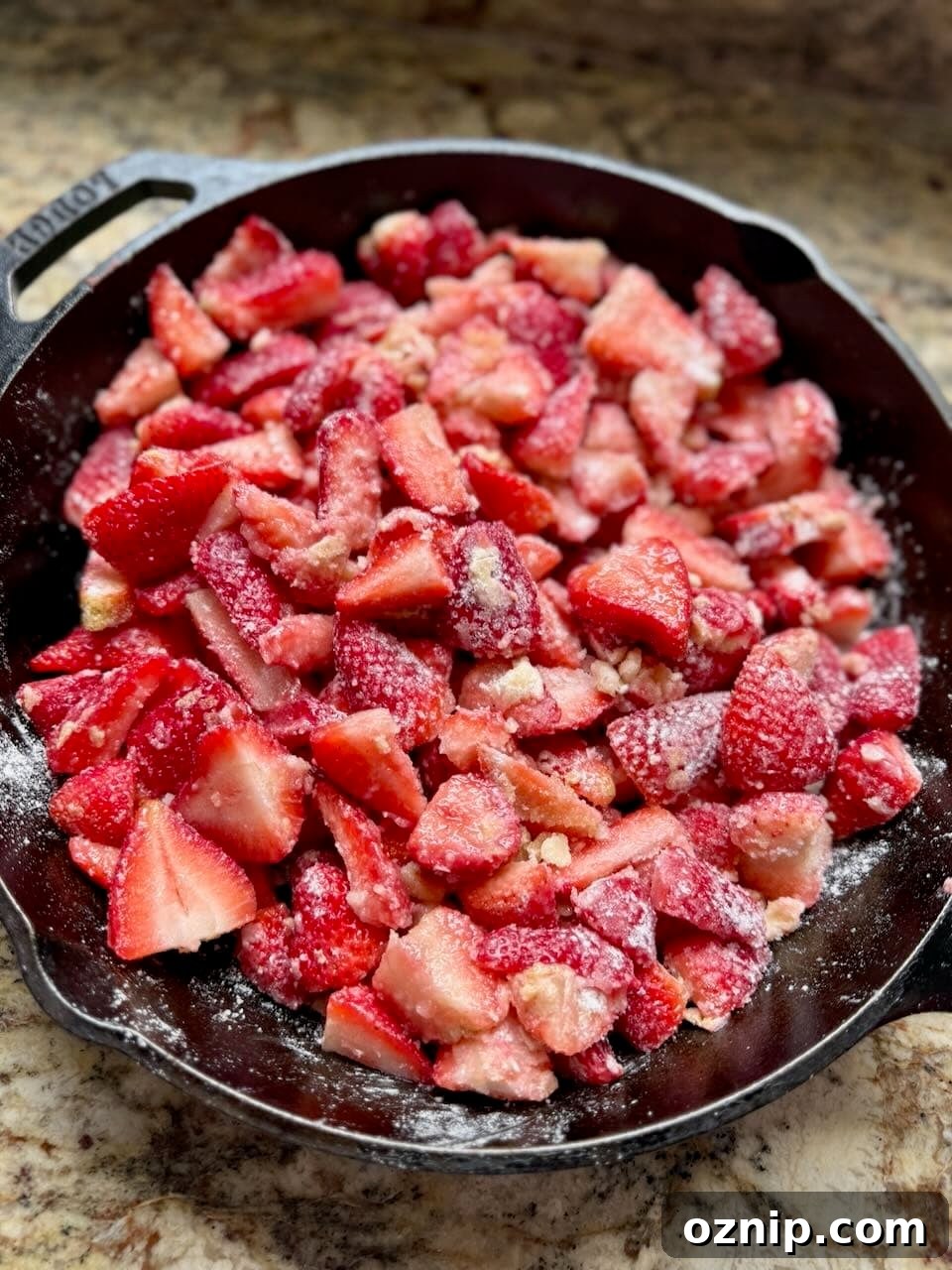Strawberries in a cast iron skillet are coated with a sugar mixture.