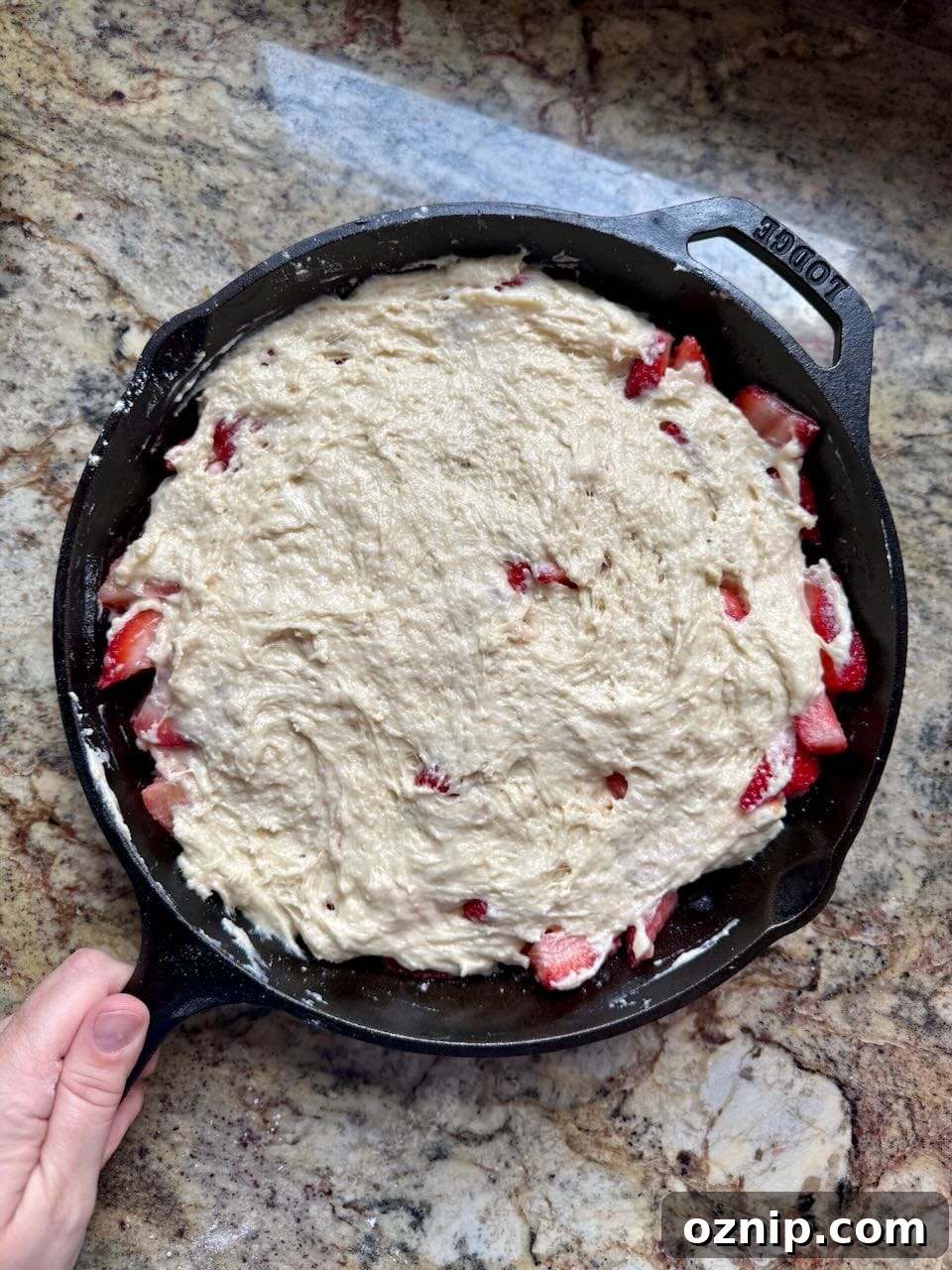 A skillet containing sliced strawberries is coated with cobbler batter.