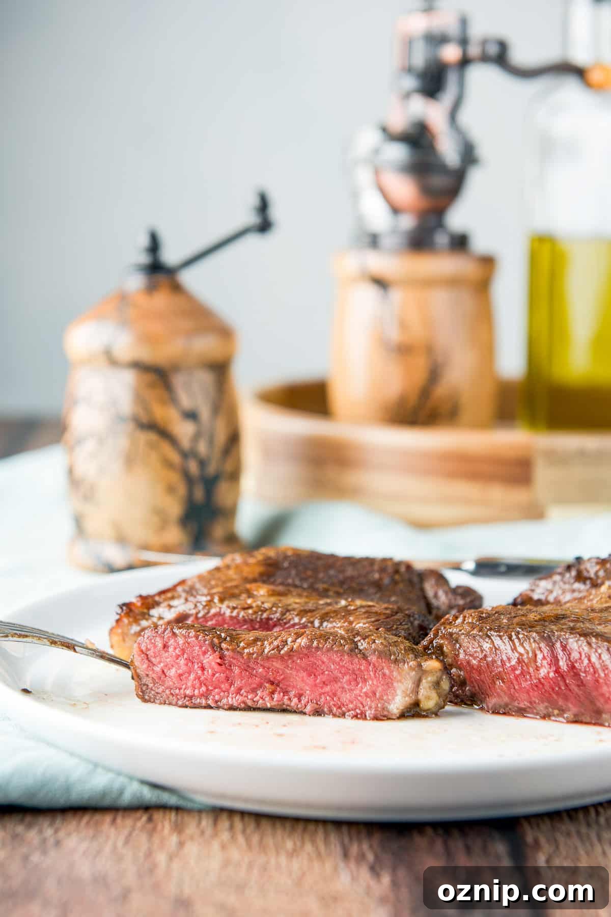 Vertical view of the medium rare steak on a white plate with condiments in the back