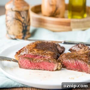 square photo of steak on a white plate cut to show that it's medium rare - with a salt and pepper mill in the background