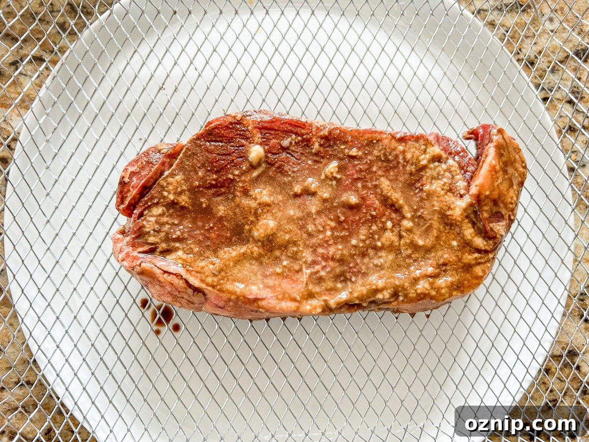 A raw steak on the air fryer basket tray over a white plate