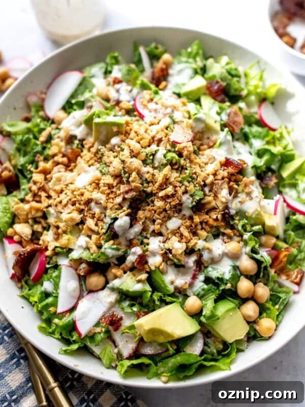 White ceramic bowl with Avocado Caesar Salad with lemon tahini salad dressing and gold forks to the side.