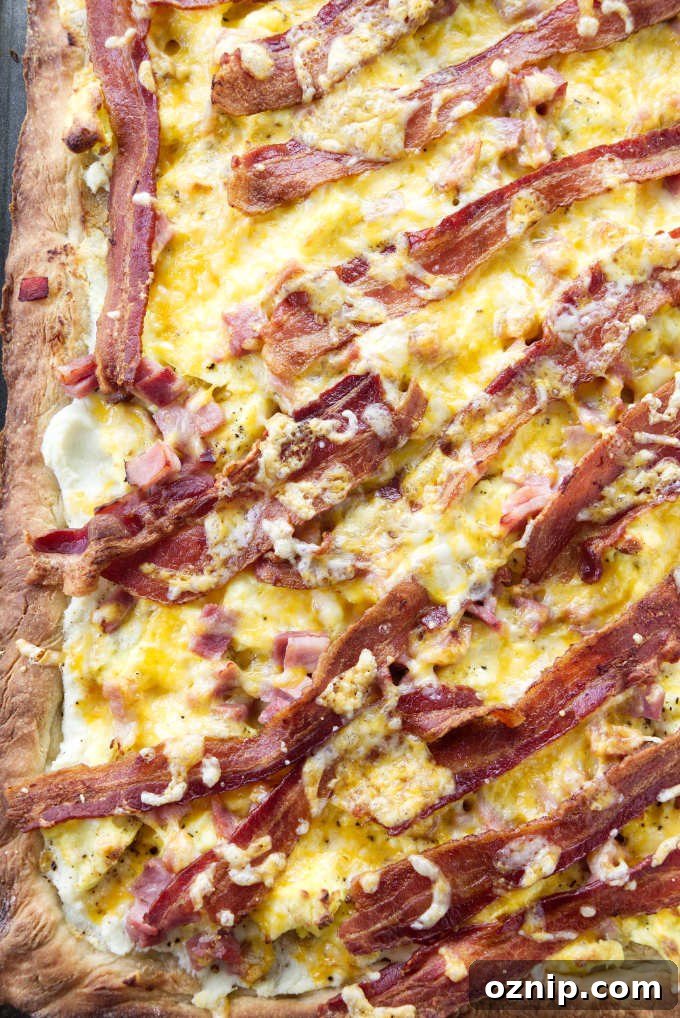 A sheet pan breakfast pizza with bacon, eggs, ham, and cheese.