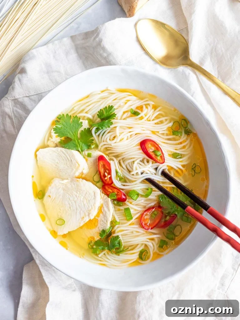 Asian chicken noodle soup with red peppers and herbs in a white bowl with chopsticks and a spoon
