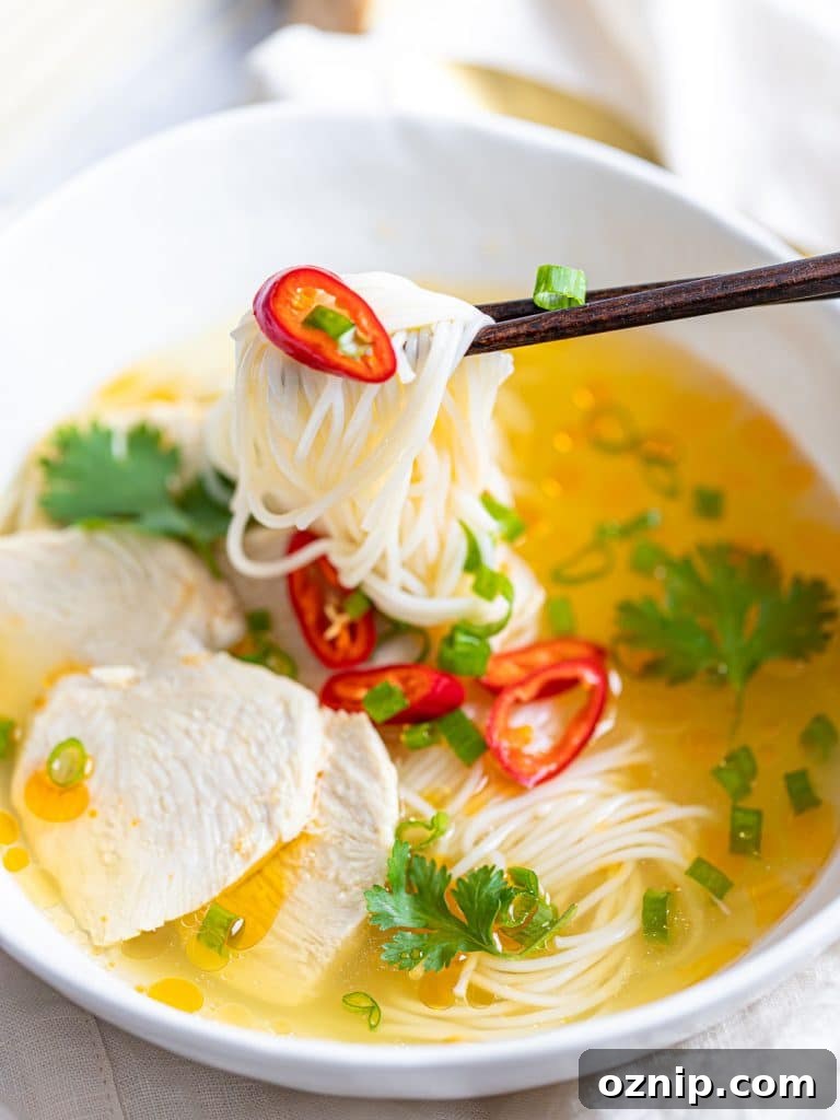 Asian chicken noodle soup with red peppers and herbs in a white bowl with chopsticks