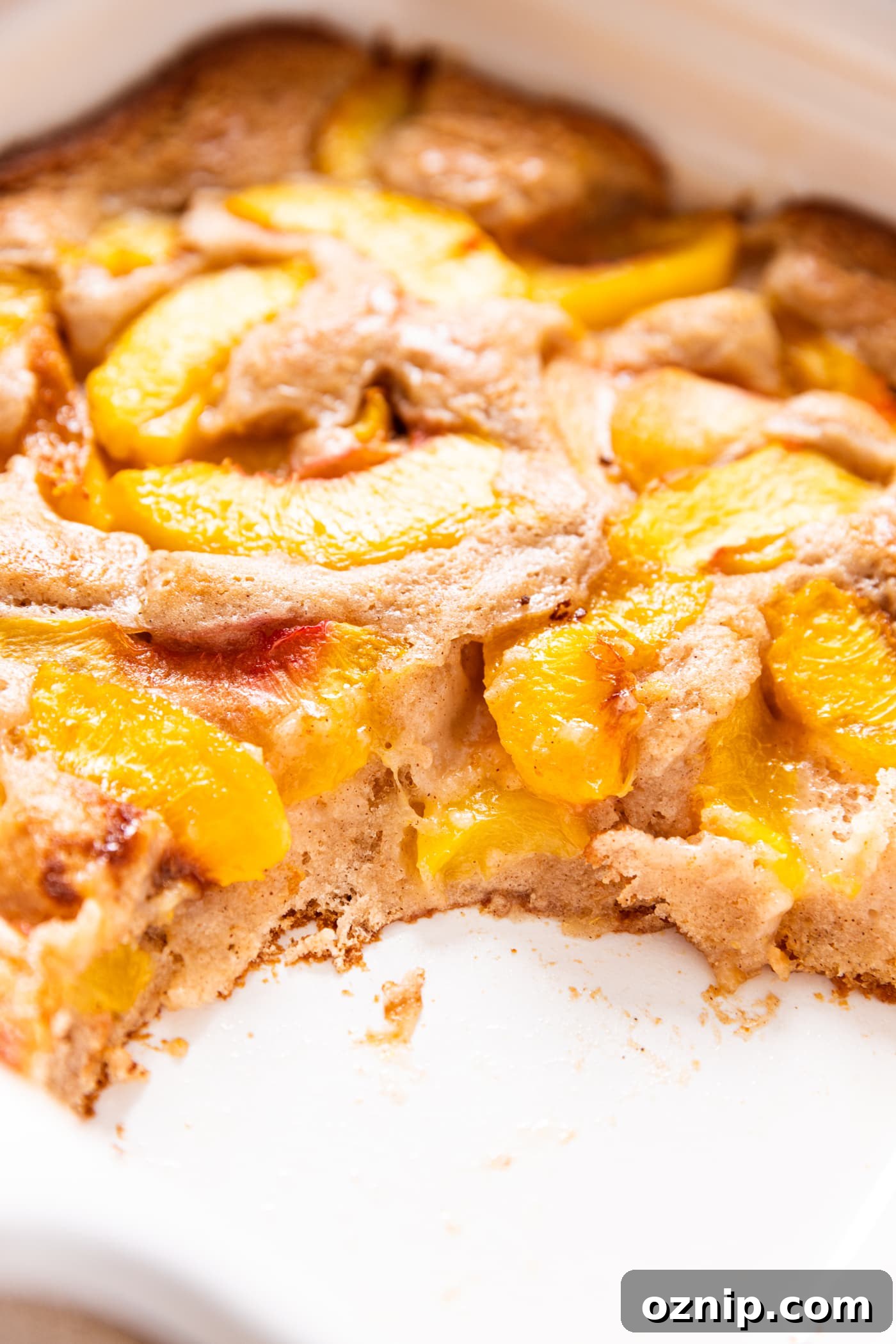 Peach cobbler sitting in white dish with scoops taken out of it showing interior of cobbler.