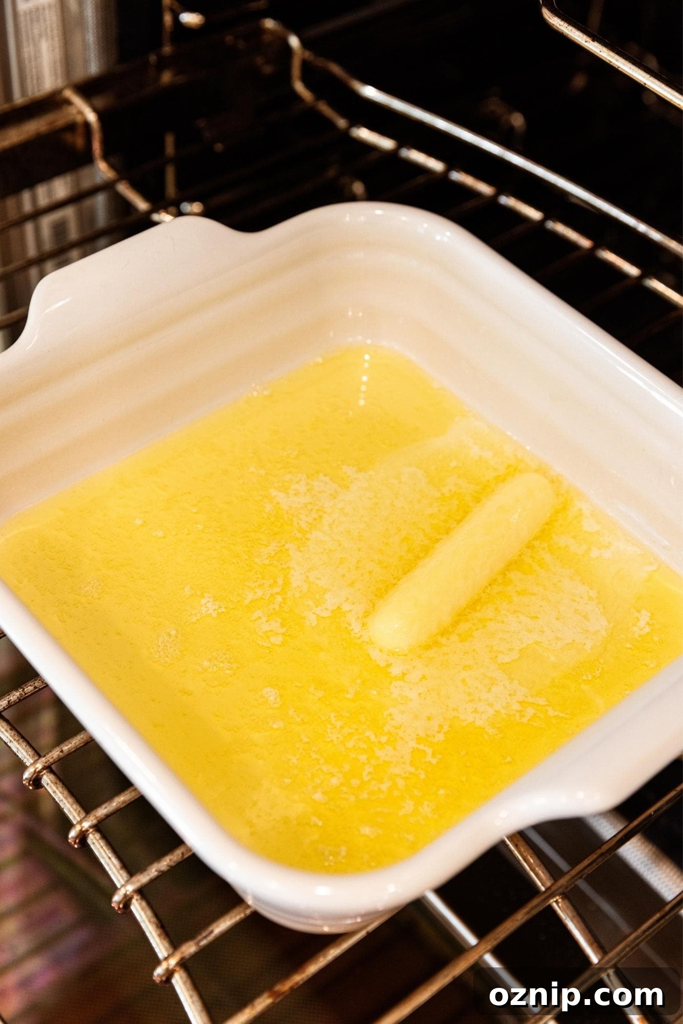 Melted stick of butter in white baking dish sitting on wire rack in open oven.