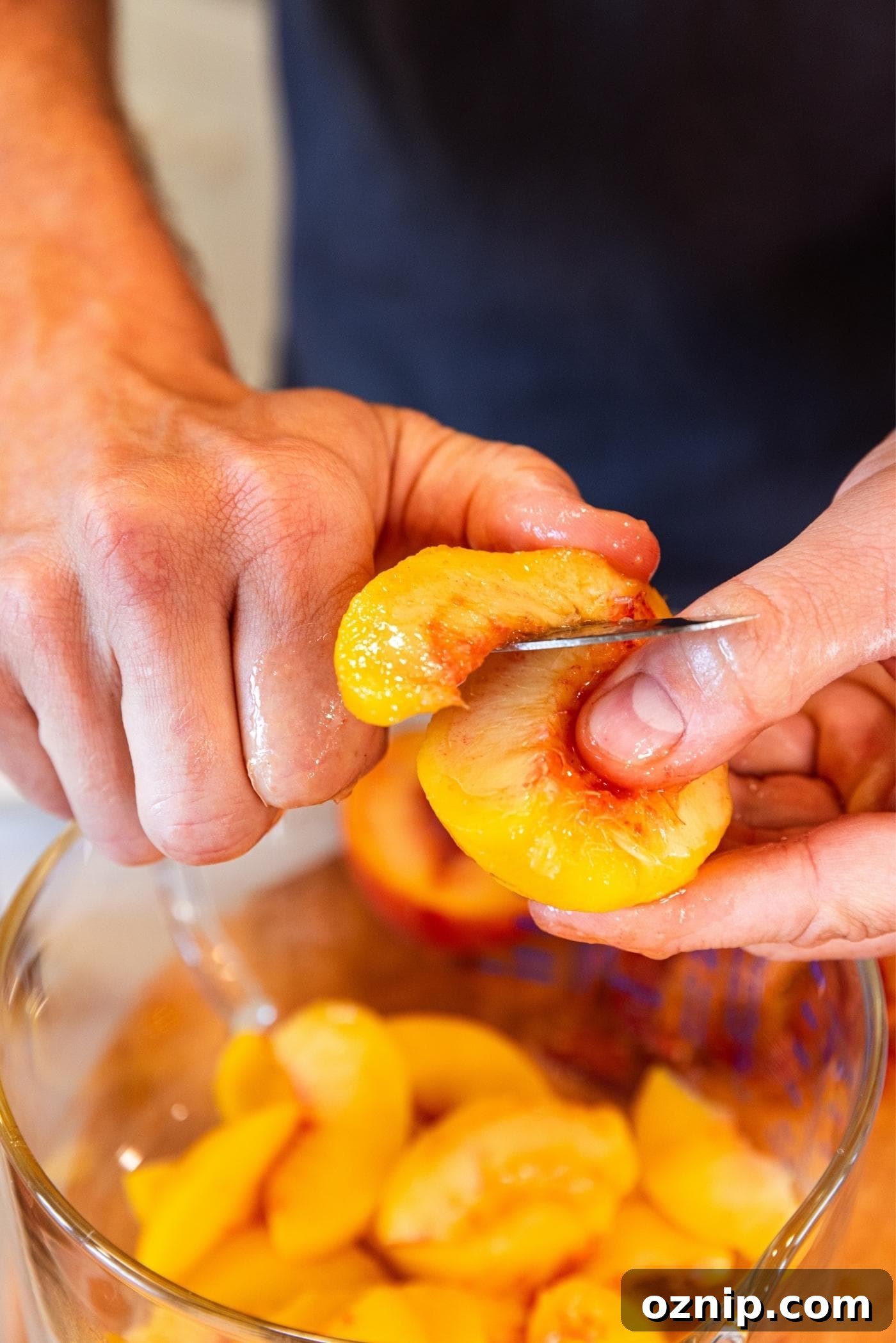 Two hands holding a peach slicing it into small slices.