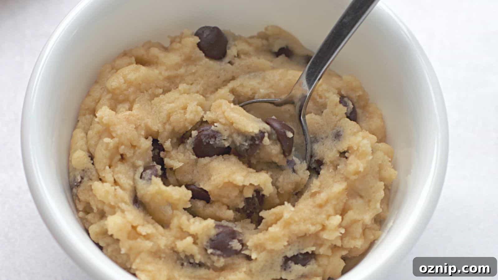 A bowl of raw cookie dough with chocolate chips and a spoon.