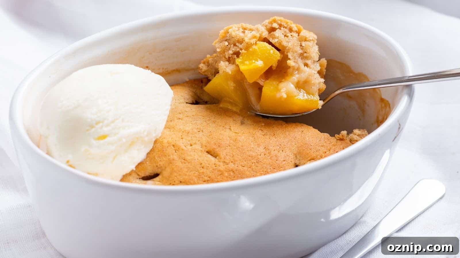 A scoop of vanilla ice cream beside a spoonful of warm peach cobbler in a white dish.