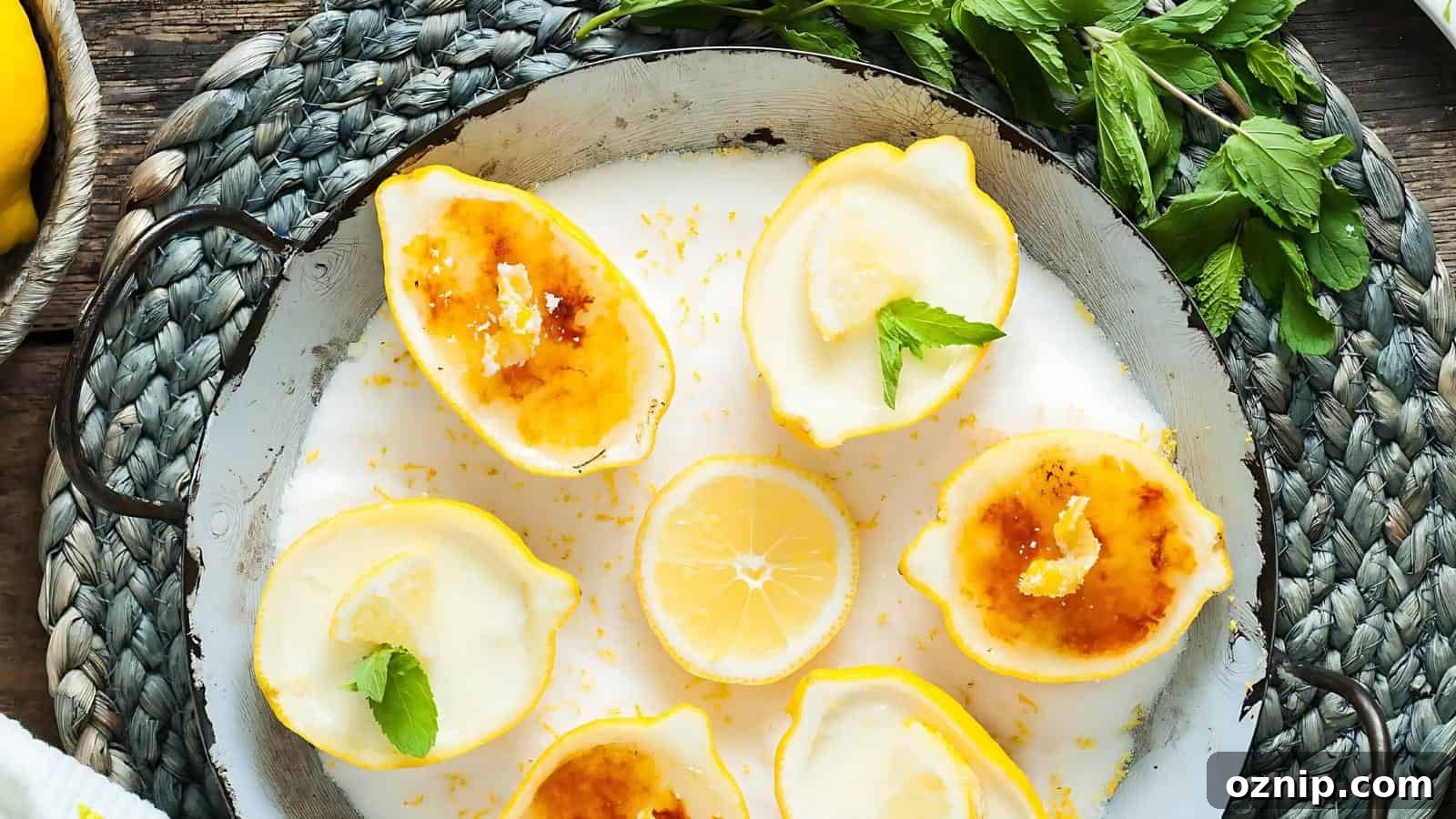 Halved lemons filled with a creamy dessert, some topped with caramelized sugar and mint leaves, arranged on a white plate with a sliced lemon and fresh mint nearby.