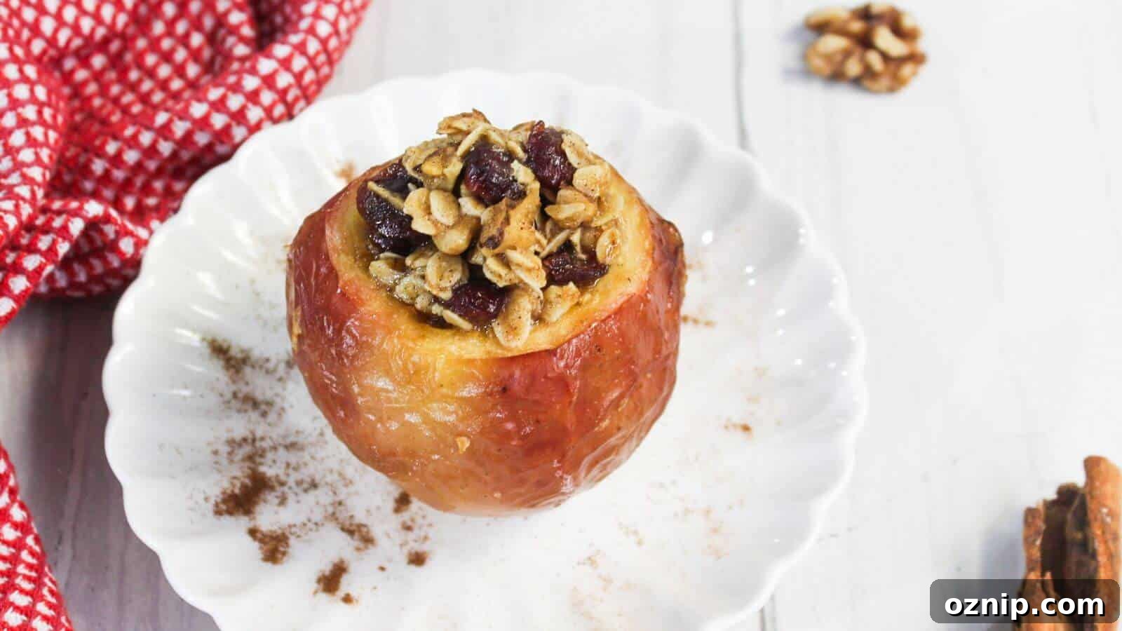 Baked apple in air fryer filled with oats and dried fruit on a white plate, next to a red-checkered cloth and cinnamon sticks.