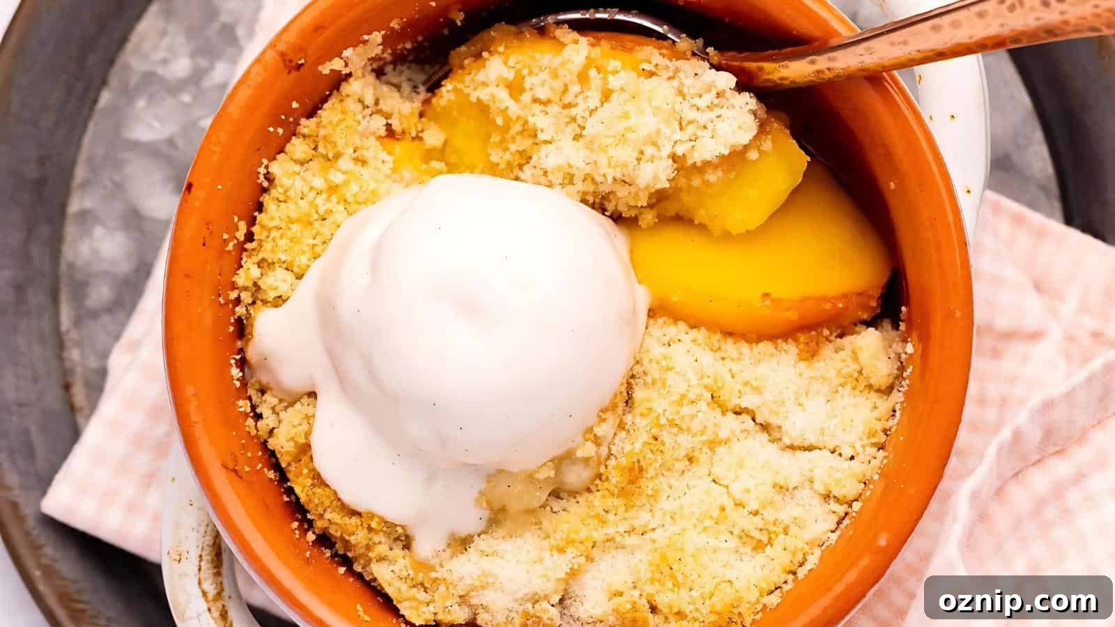 A baked peach crumble dessert in a small clay dish, topped with a scoop of vanilla ice cream and served with a spoon.