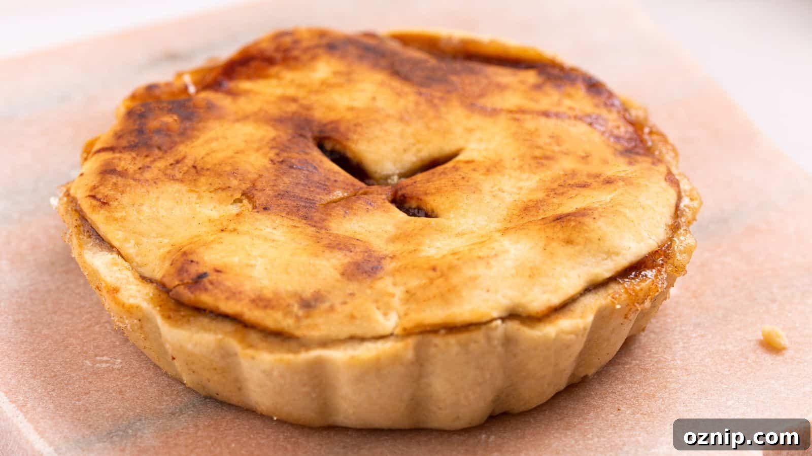 Golden-brown baked apple pie with a flaky crust and a cutout in the center, served on a beige surface.