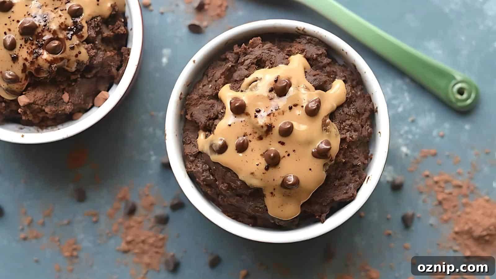 A white ramekin filled with chocolate mug cake topped with peanut butter and chocolate chips, placed on a blue surface with scattered cocoa powder and chocolate chips.
