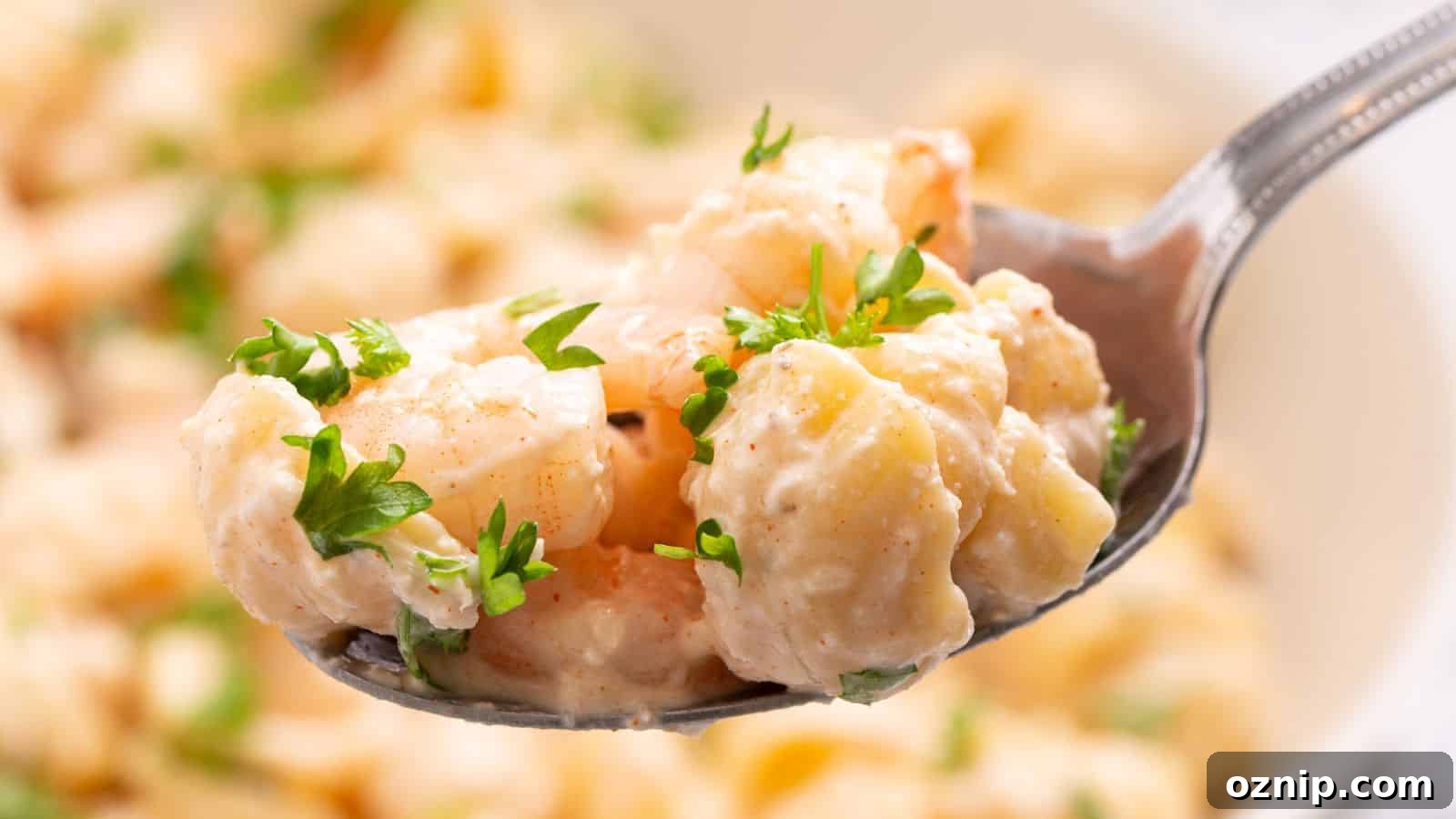 Close-up of a spoon holding seafood pasta salad garnished with parsley, with more salad in the background.