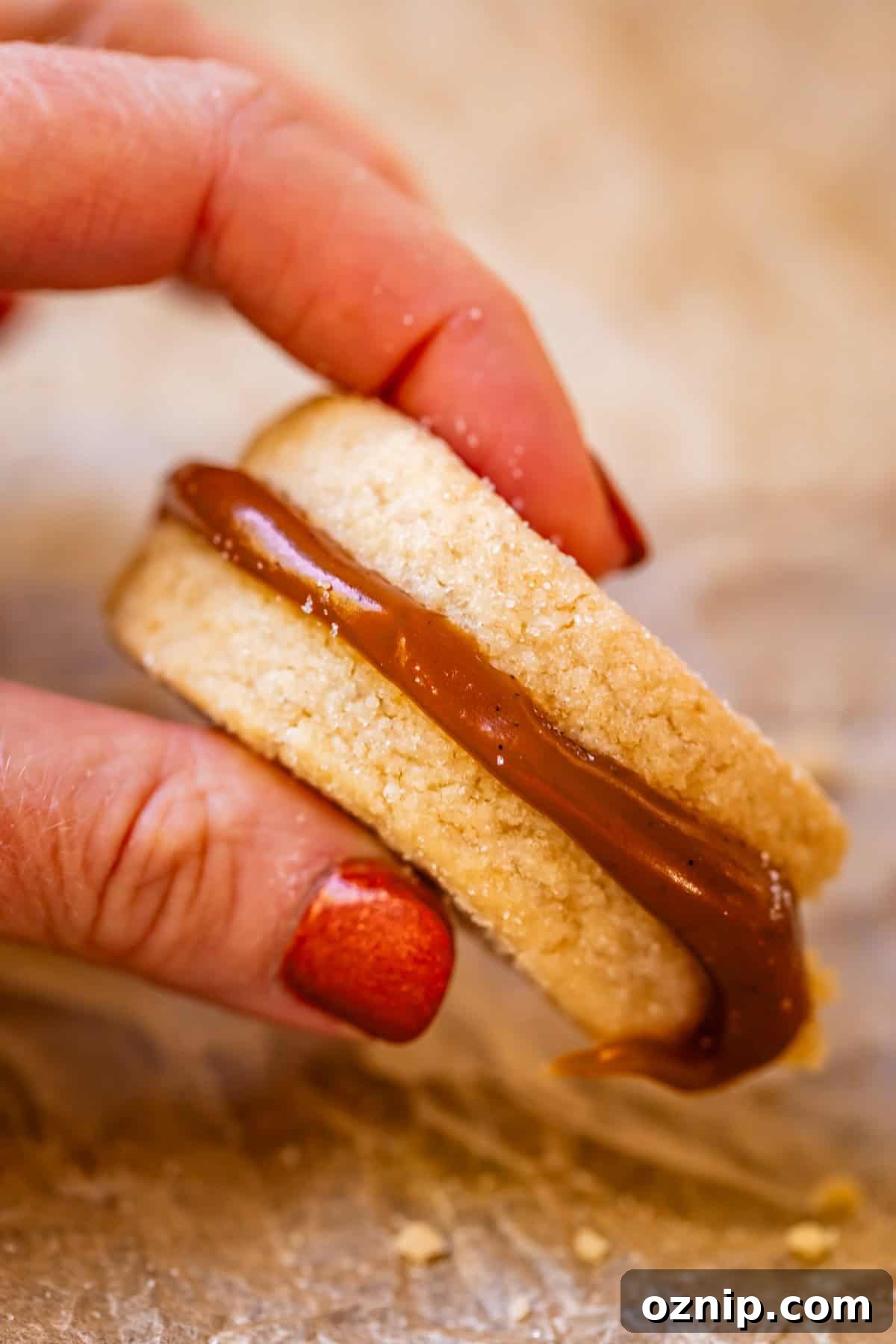 Classic Homemade Buttery Shortbread Cookies 15 fingers holding up shortbread sandwich cookie with caramel in the center.