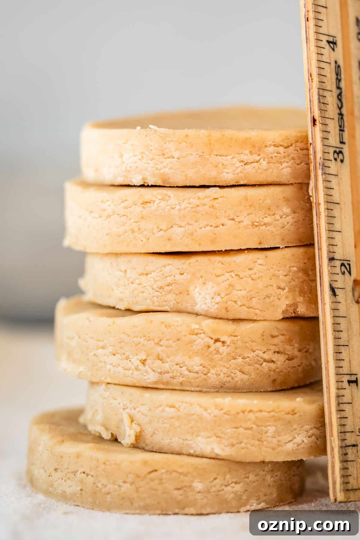 Classic Homemade Buttery Shortbread Cookies 5 round raw cookies stacked with a ruler next to them showing how thick they are.