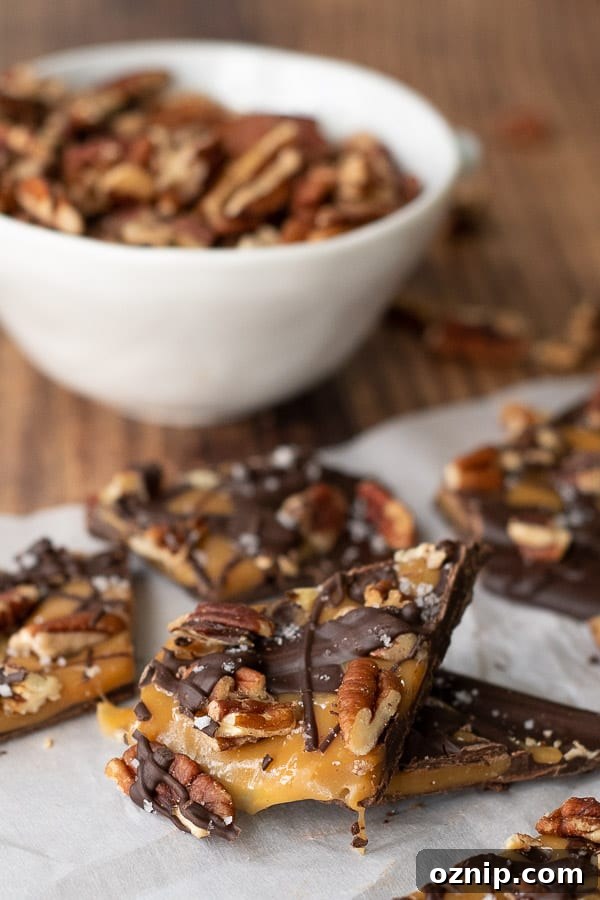 pieces of salted caramel chocolate bark on parchment with a bowl of pecans in background