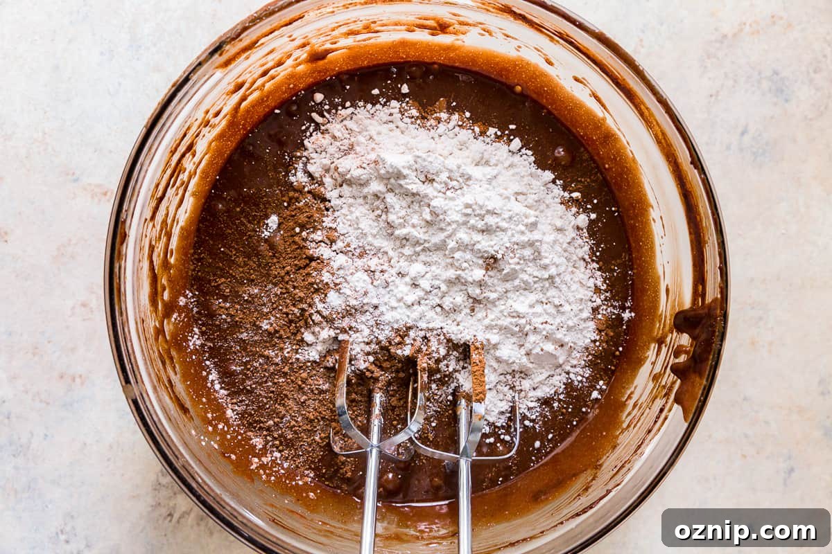 dry ingredients added to brownie batter in a glass bowl