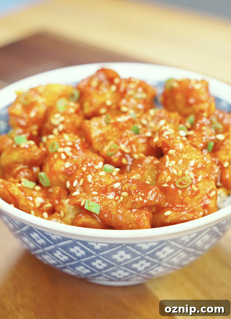Finished bowl of Crispy Gochujang Chicken coated in a glossy sweet and spicy gochujang glaze and garnished with sesame seeds and scallions. This easy air fryer chicken recipe delivers restaurant-quality flavor with a crispy exterior and tender juicy chicken.