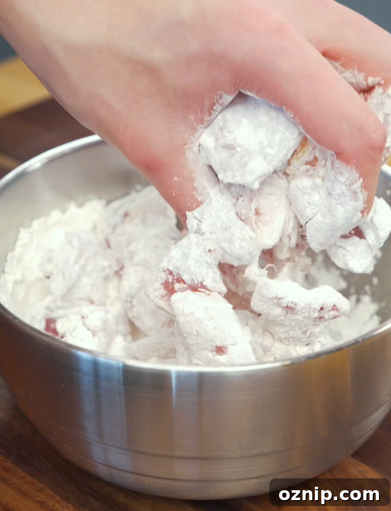 Chicken thigh pieces being coated in a mixture of cornstarch, flour, and salt before air frying. This light dredge helps create the crispy texture that makes this Crispy Gochujang Chicken Recipe so satisfying.