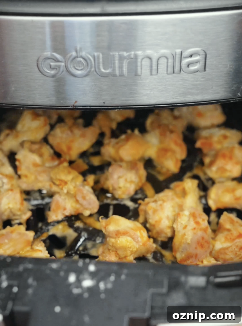 Chicken thighs cooking inside an air fryer until golden brown and crispy. Air frying creates crunchy chicken pieces with less oil while keeping the inside tender and juicy.